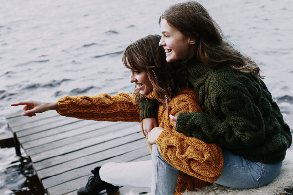 two girls look happily out to the water while sitting on a dock